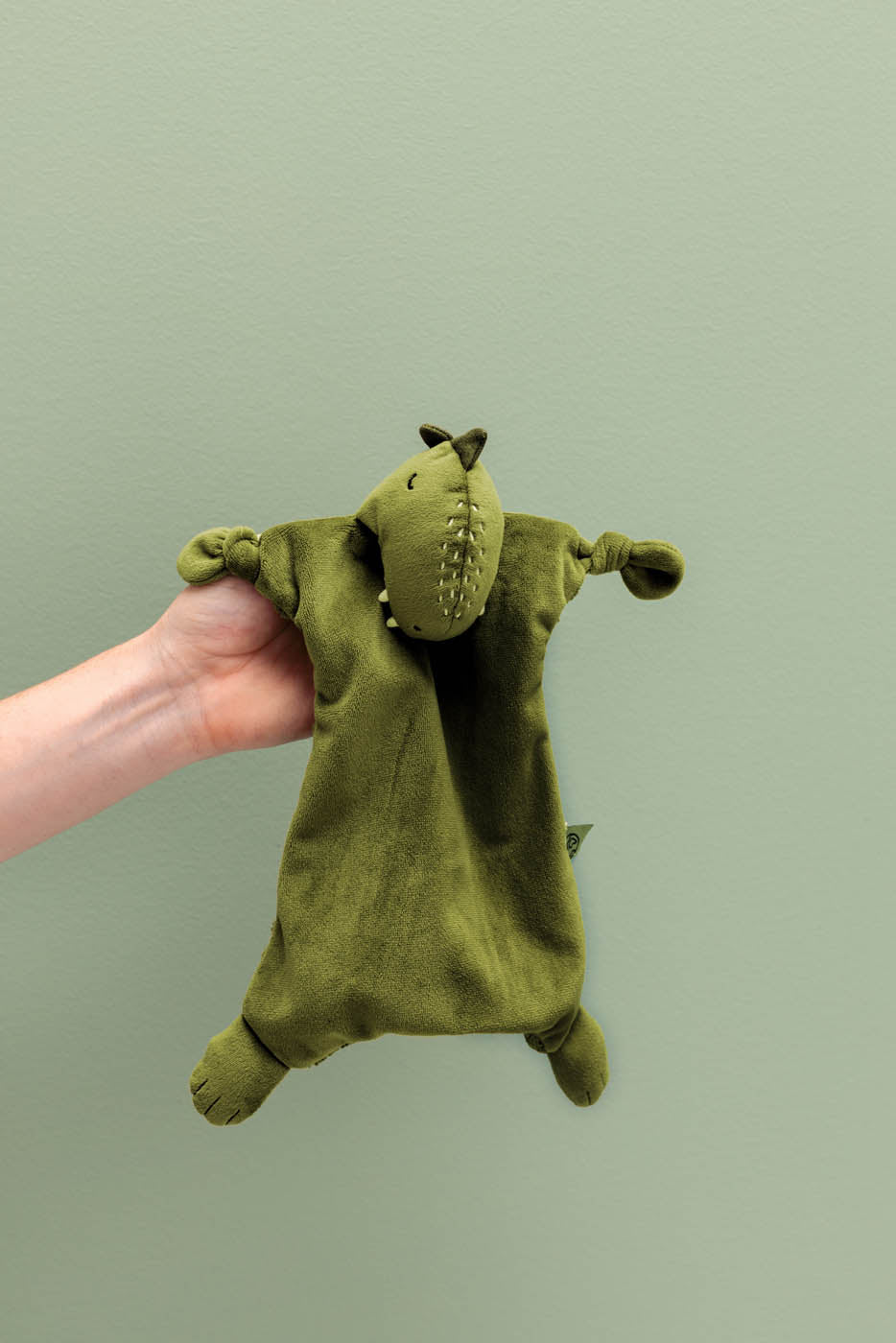 Doudou Mr. Dino Trixie tenu à la main sur fond vert