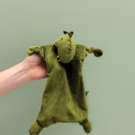 Doudou Mr. Dino Trixie tenu à la main sur fond vert